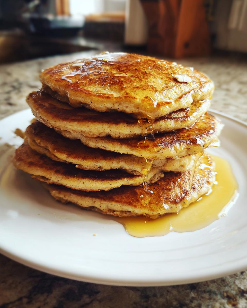 A stack of banana oatmeal pancakes on a white plate, drizzled with syrup. Delicious banana oatmeal pancakes!