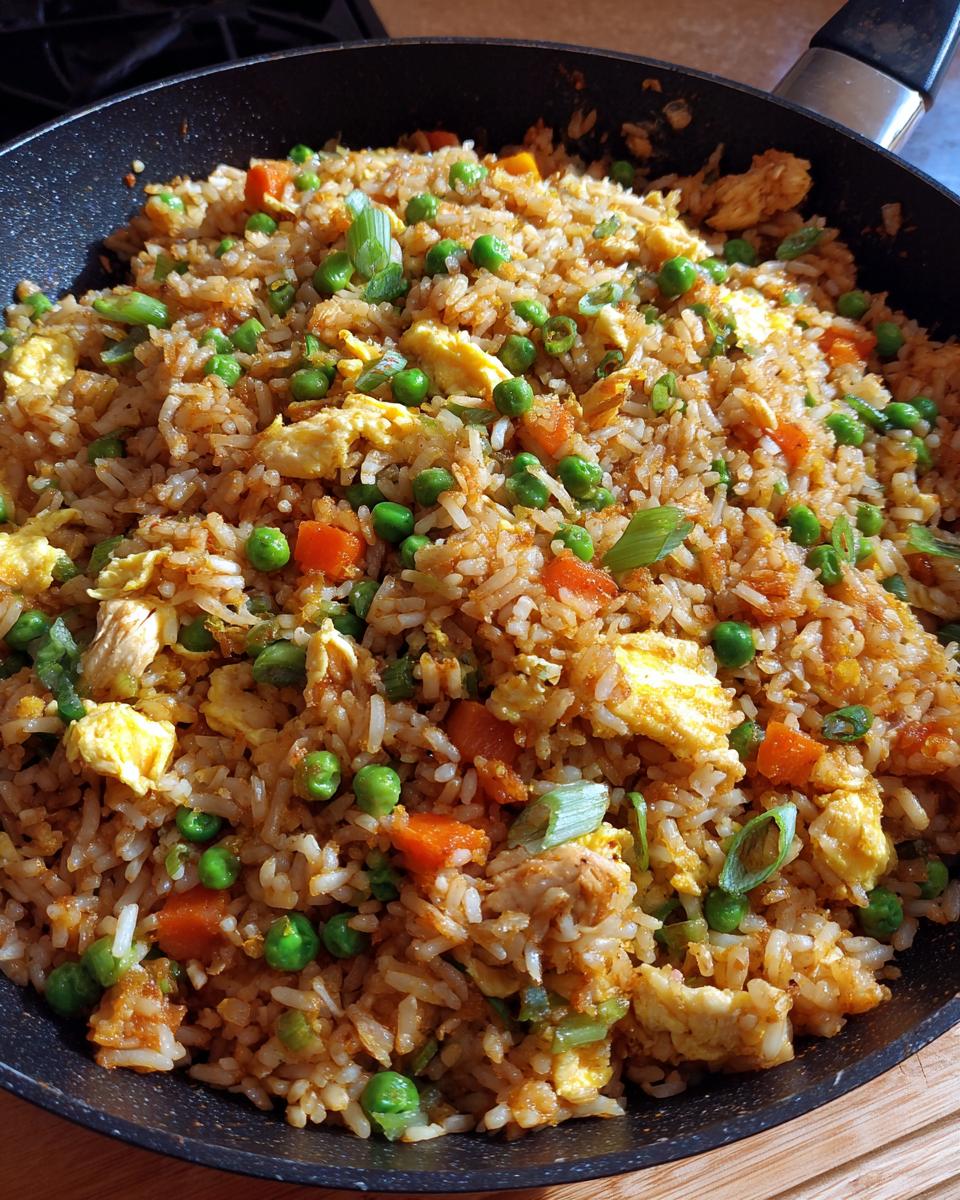Overhead view of freshly made Chicken fried rice in a pan, featuring peas, carrots, and egg.