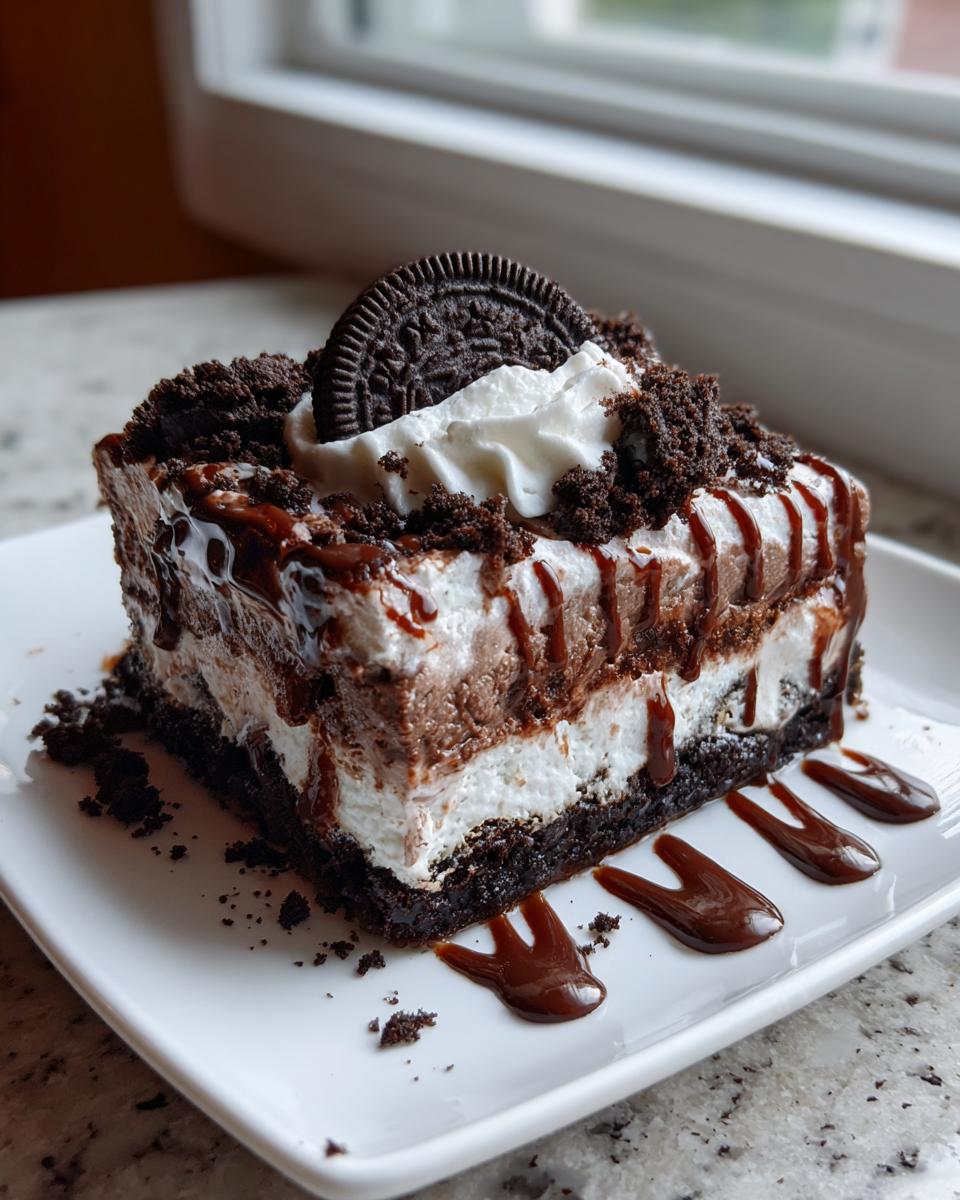 A slice of chocolate lasagna dessert with layers of cream and chocolate, topped with an Oreo cookie.
