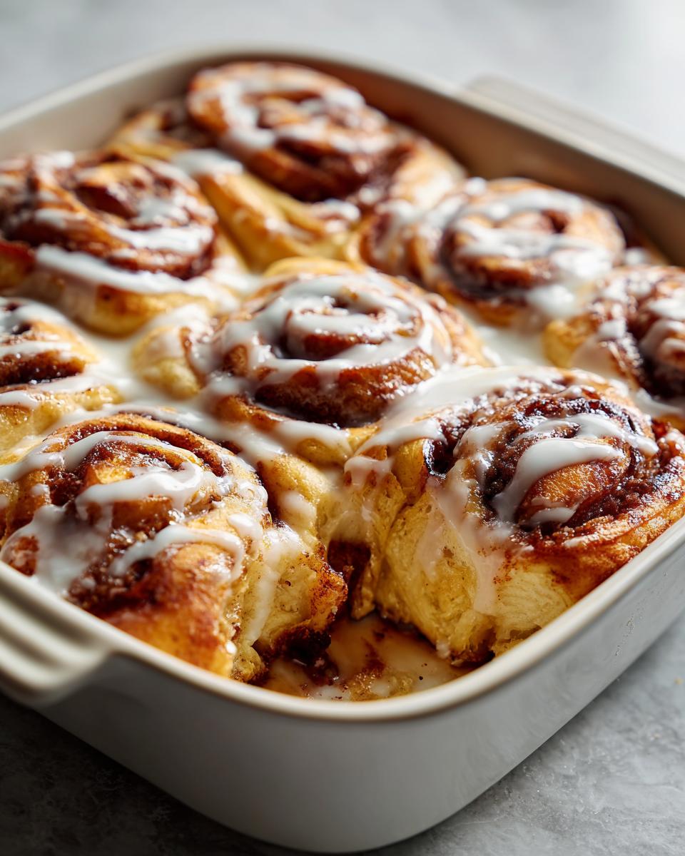Close up of a freshly baked cinnamon roll casserole with white icing in a square baking dish.