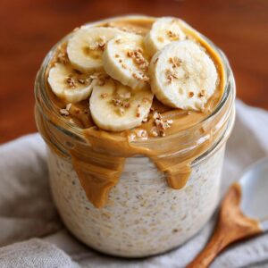 Jar of peanut butter banana overnight oats topped with banana slices and peanut butter drizzle.