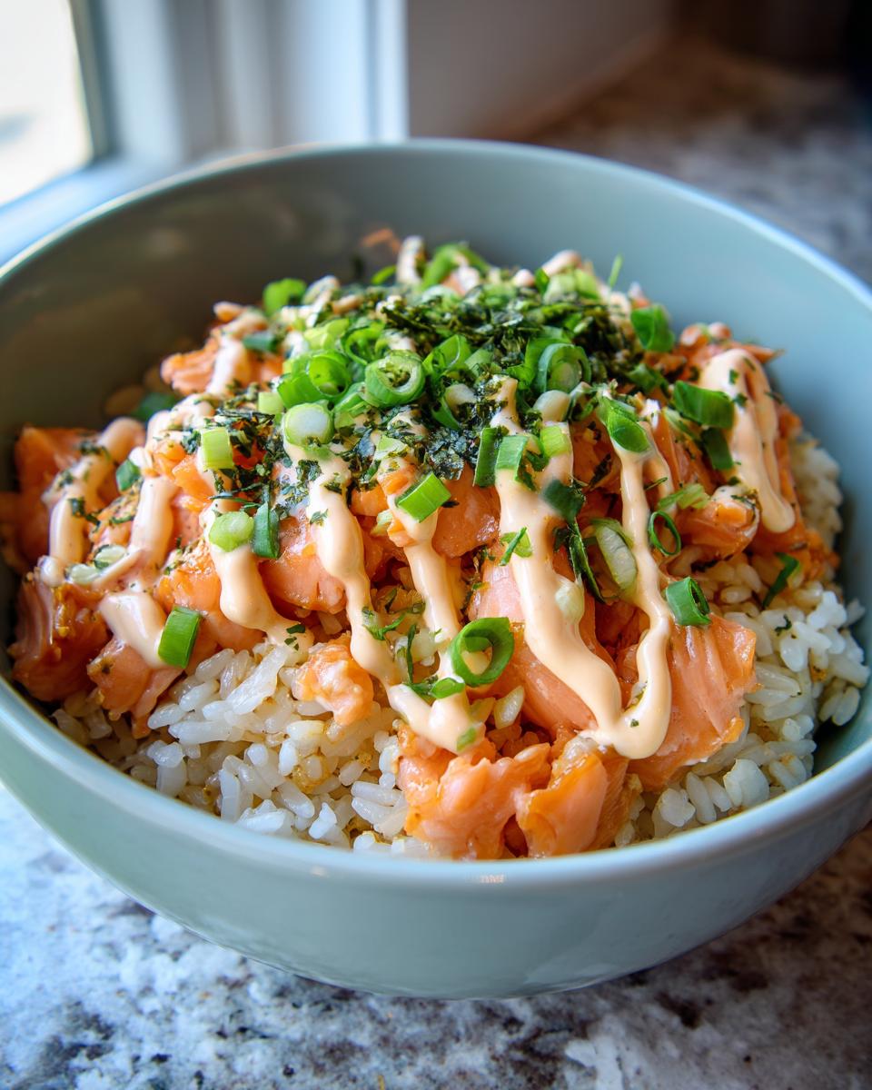 A vibrant salmon rice bowl with sauce, green onions, and nori flakes in a blue bowl.