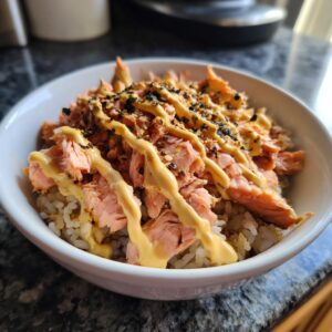 A flavorful salmon rice bowl topped with sauce and seasoning, ready to eat.