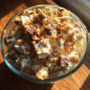 A bowl of Snickers apple salad with apples, Snickers pieces, whipped cream, and caramel drizzle.