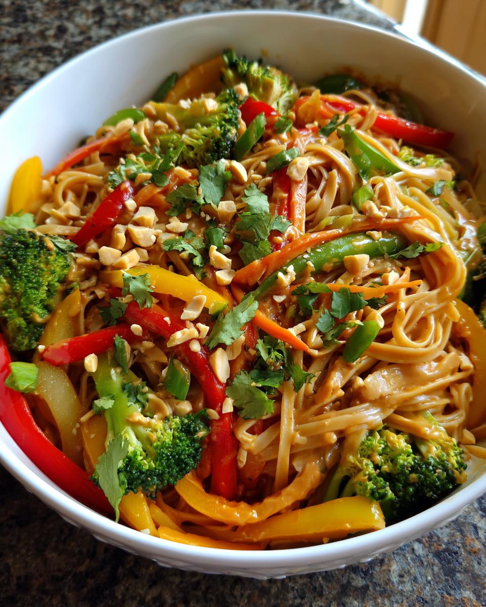 Close-up of Thai peanut noodles with vegetables, including broccoli, peppers, and carrots, topped with peanuts and cilantro.