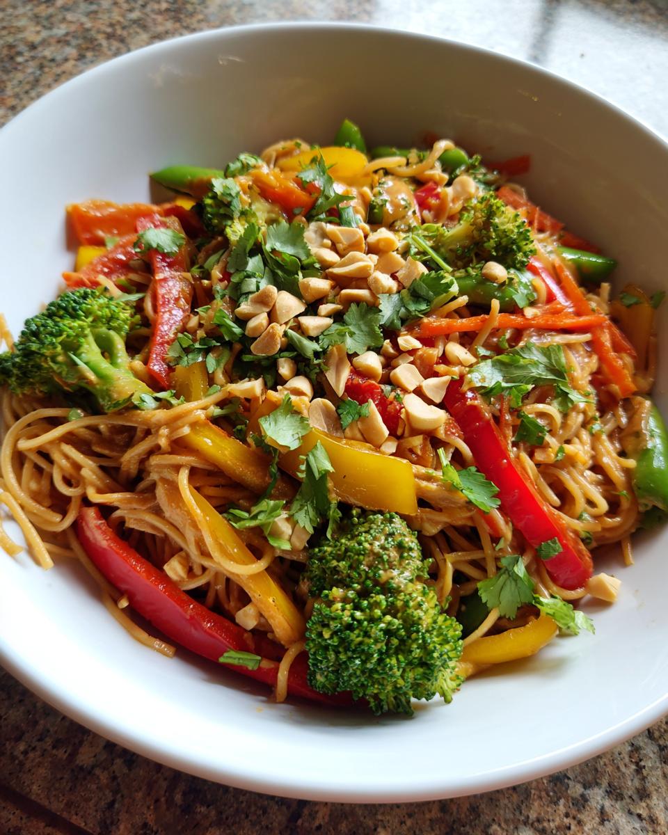 A vibrant bowl of Thai peanut noodles with vegetables, garnished with peanuts and cilantro.