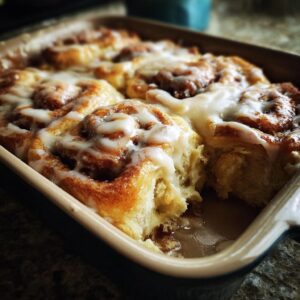 Freshly baked TikTok cinnamon rolls with creamy icing in a baking dish, one roll partially eaten.
