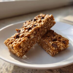 Two Chewy Peanut Butter Granola Bars stacked on a white plate, topped with chocolate chips.