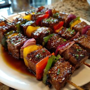Delicious Grilled Teriyaki Steak Skewers with colorful bell peppers and red onions on a white plate.