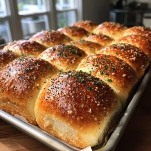 Close-up of baked Ham and Cheese Hawaiian Roll Sliders on a baking sheet, topped with herbs and seasonings.