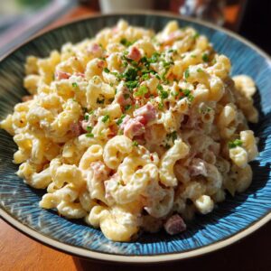 Close-up of Hawaiian Macaroni Salad in a blue bowl, garnished with chives and ham.