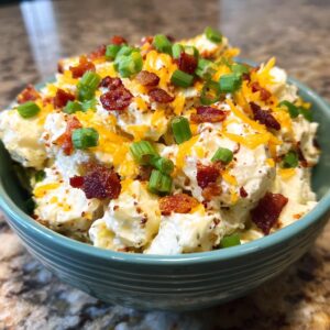 A bowl of Loaded Baked Potato Salad topped with bacon, cheese, and green onions.