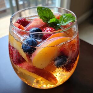 A glass of Peach Sangria filled with peach slices, blueberries, strawberries, and garnished with fresh mint.