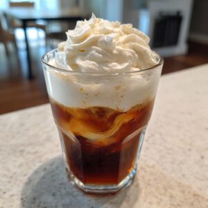 A glass of Pumpkin Cream Cold Brew Copycat topped with whipped cream, showcasing the drink's layers.