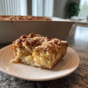 A close-up of a slice of Apple Cinnamon French Toast Bake on a white plate, showcasing the tender apple pieces and crumb topping.