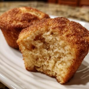 A close-up of two tender Apple Cinnamon Muffins on a white plate, one with a bite taken out.
