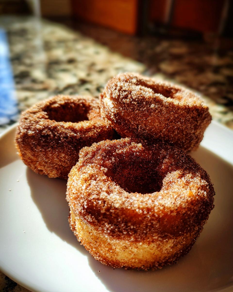 Close-up of three baked apple cider donuts coated in cinnamon sugar on a white plate.
