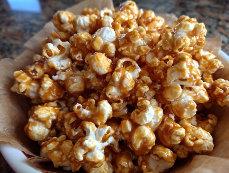 A close-up of a bowl overflowing with delicious caramel popcorn, coated in a glossy caramel sauce.