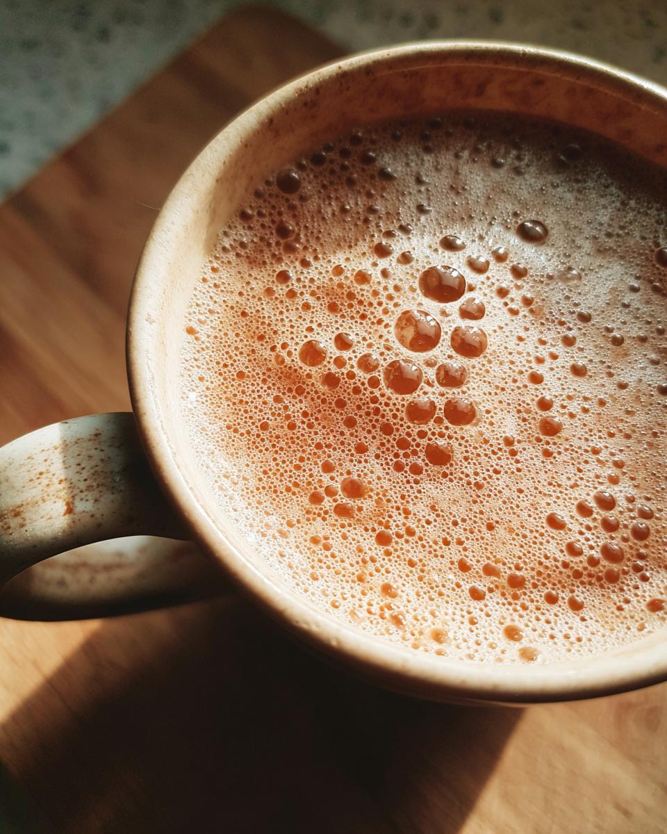 Close-up of a frothy, bubbly chai latte in a rustic mug, bathed in warm sunlight.