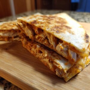 Close-up of a golden-brown chicken quesadilla, cut into wedges and stacked, revealing shredded chicken and melted cheese.