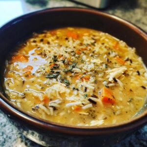A close-up of a warm bowl of chicken wild rice soup, featuring shredded chicken, rice, carrots, and herbs.