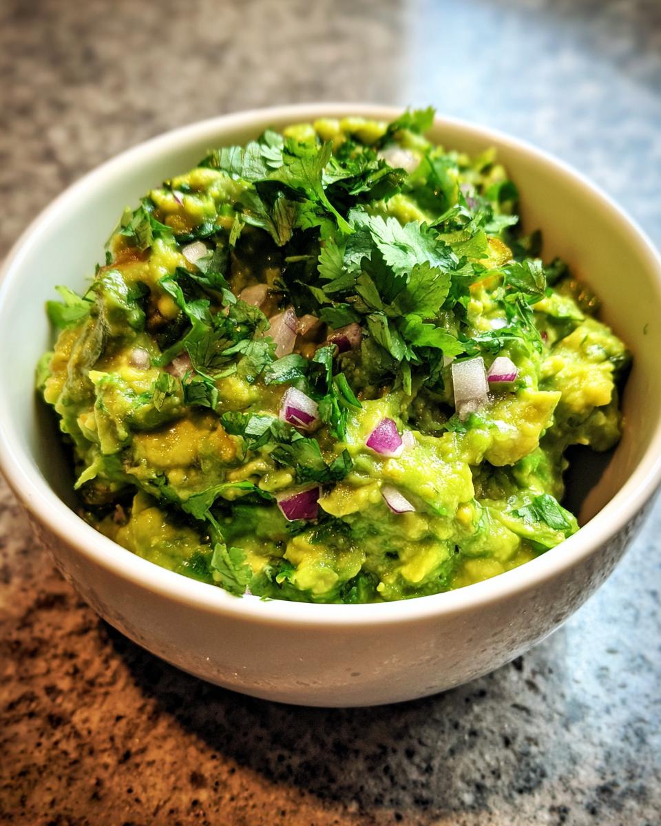 A close-up of a bowl filled with vibrant green classic guacamole, topped with fresh cilantro and diced red onion.
