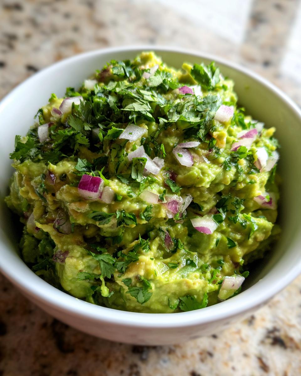 A bowl of chunky Classic Guacamole topped with fresh cilantro and diced red onion.