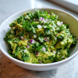 A close-up of a bowl of fresh Classic Guacamole, topped with chopped cilantro and red onion.