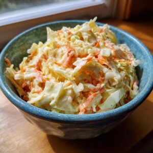 A close-up of creamy coleslaw with shredded cabbage and carrots in a blue bowl.