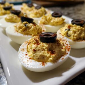 Close-up of Ghoulish Deviled Egg Eyeballs topped with black olive slices and paprika.