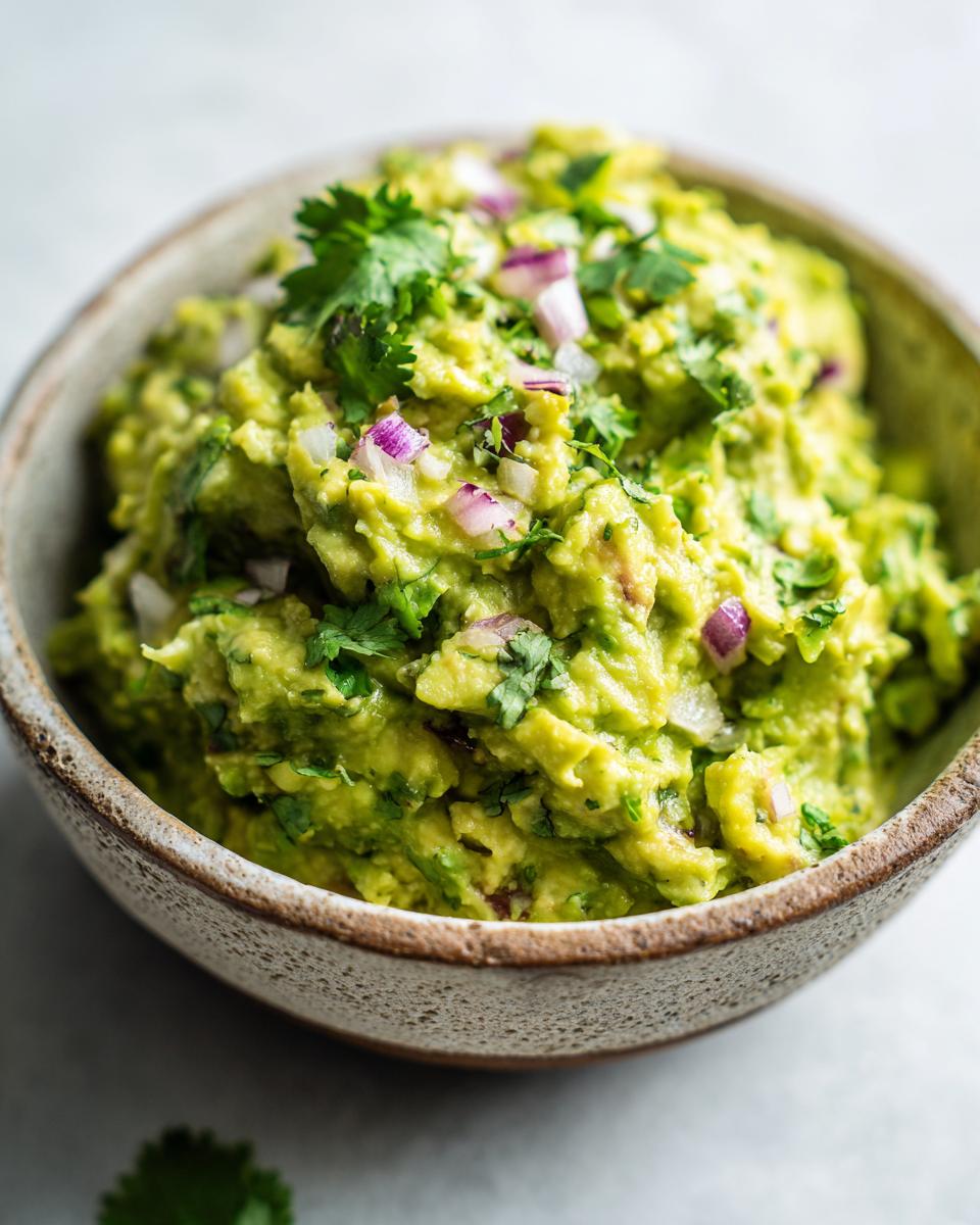 A close-up of a bowl of fresh guacamole, topped with chopped red onion and cilantro.