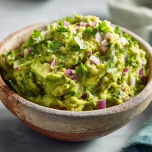 A close-up of a rustic bowl filled with vibrant green guacamole, topped with chopped cilantro and red onion.
