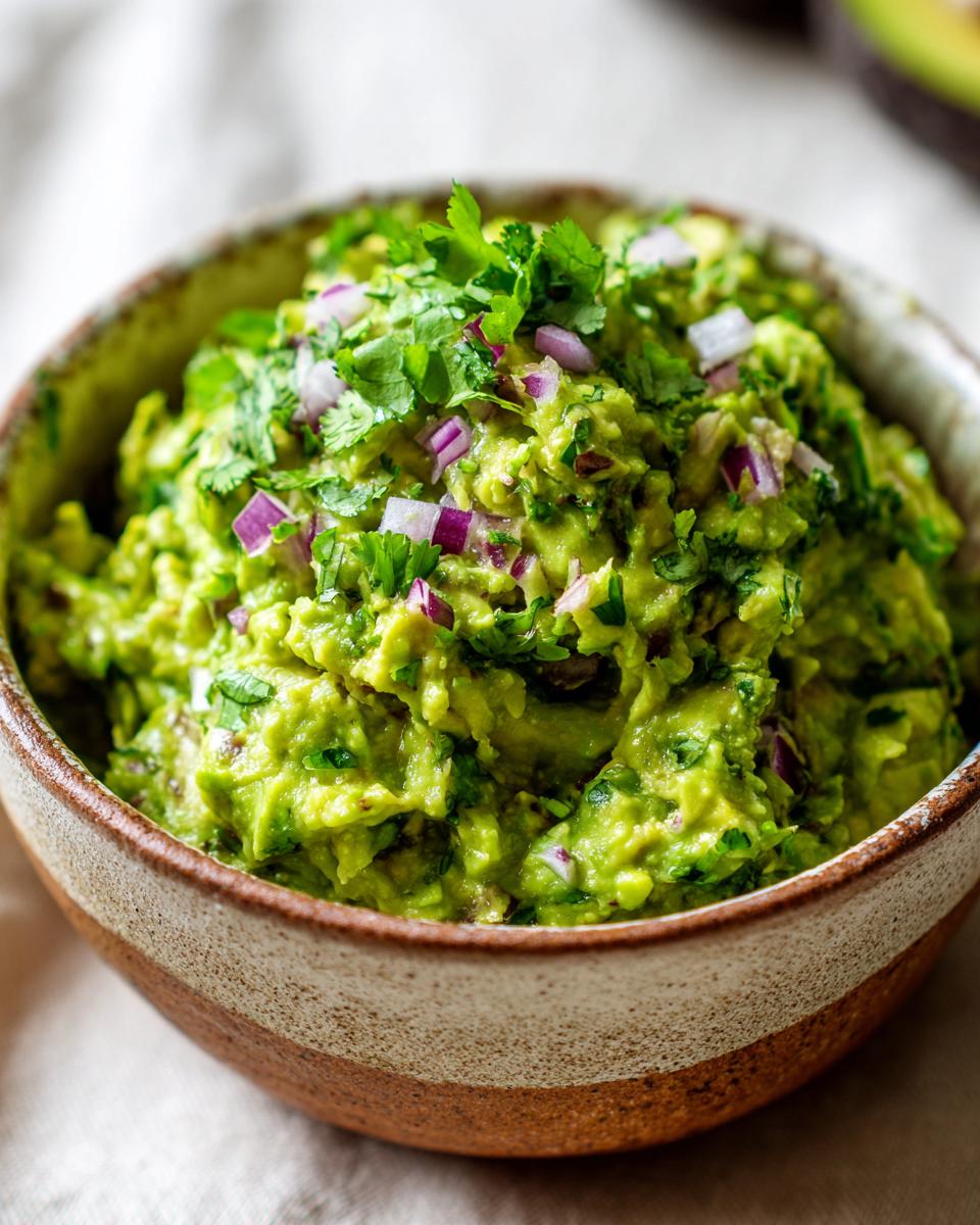 A close-up of a bowl of freshly made guacamole, topped with chopped cilantro and red onion.
