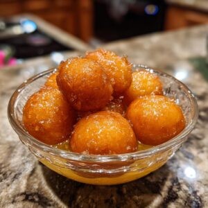 Close-up of sweet, golden-brown Gulab Jamun balls soaked in syrup in a glass bowl.