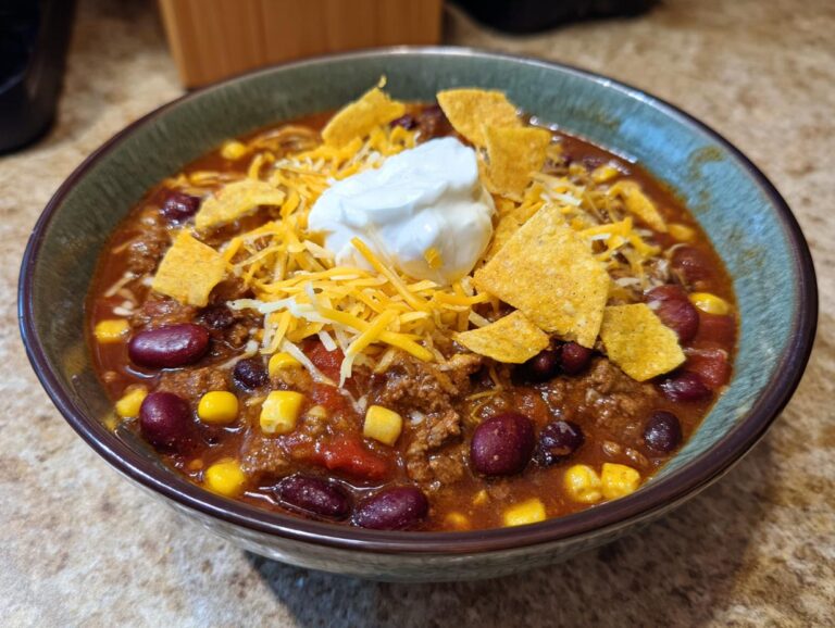 A close-up of a bowl of hearty taco soup, topped with shredded cheese, tortilla chips, and sour cream.