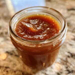 A close-up of a glass jar filled with rich, dark homemade apple butter.