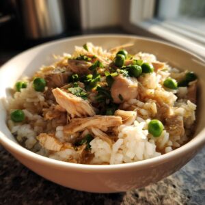 A close-up of a bowl of Instant Pot Chicken and Rice, topped with shredded chicken, green peas, and fresh parsley.
