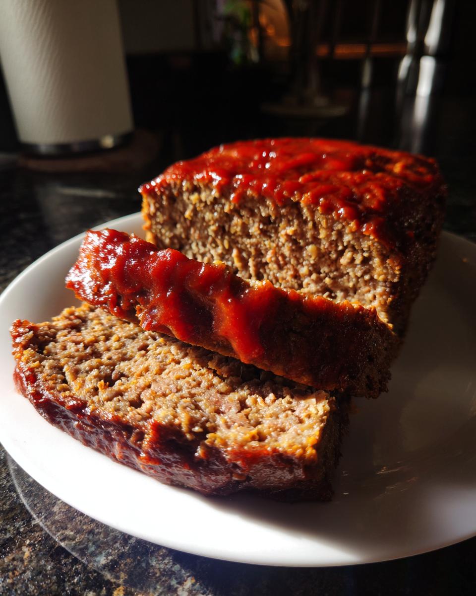 A close-up of a sliced meatloaf with a glossy red glaze on a white plate.