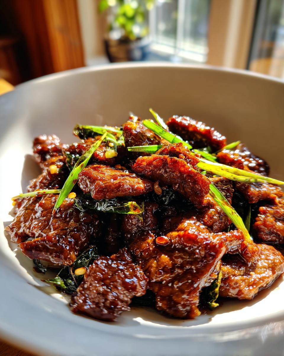 A close-up of a bowl filled with glistening Mongolian beef, garnished with green onions.