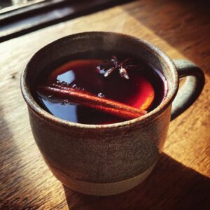 Close-up of a steaming mug of mulled wine, garnished with a cinnamon stick, star anise, and orange slice.