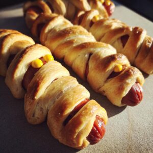 Close-up of golden-brown mummy hot dogs wrapped in pastry dough with mustard eyes.