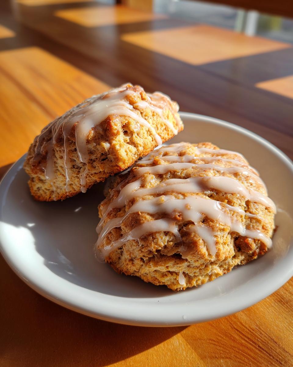Two fluffy pumpkin scones topped with a sweet maple glaze, presented on a white plate.