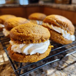 Close-up of soft pumpkin whoopie pies filled with creamy frosting on a cooling rack.