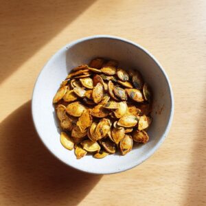 A bowl filled with golden-brown, seasoned roasted pumpkin seeds, ready to eat.