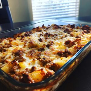 A close-up of a freshly baked sausage potato casserole in a glass baking dish, topped with melted golden cheese.