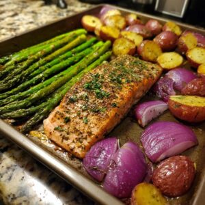 A close-up of a perfectly cooked sheet pan salmon and veggies, including asparagus, red potatoes, and red onion.