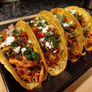 Four delicious slow cooker chicken tacos filled with shredded chicken, topped with crumbled cheese, diced tomatoes, and cilantro.
