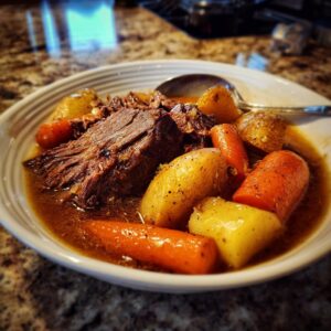 A close-up of a bowl filled with fork-tender slow cooker pot roast, tender carrots, and potatoes in savory gravy.