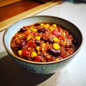 A close-up of a bowl filled with hearty vegetarian chili, featuring kidney beans, corn, and diced tomatoes.