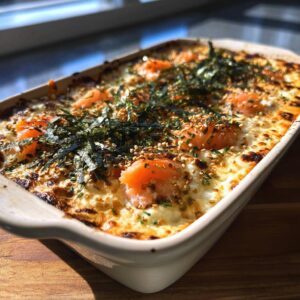 A close-up of a baked dish topped with salmon pieces, seaweed, and sesame seeds, showcasing a creamy, cheesy texture.